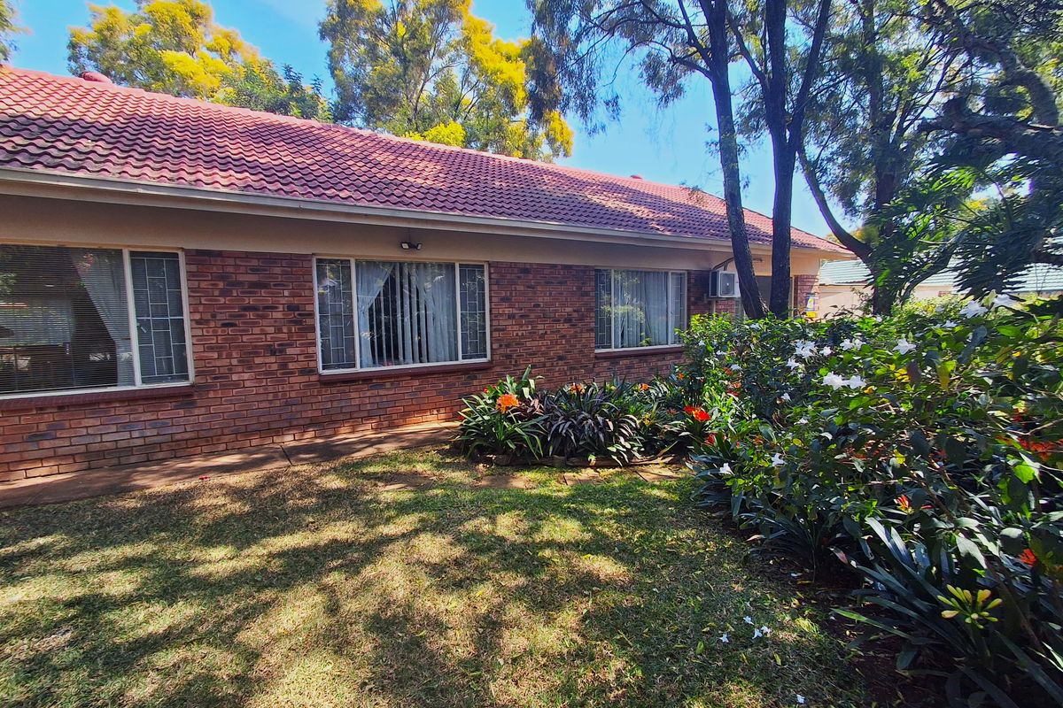Rear view of a face brick house featuring a tiled roof, established garden, and secure aluminum-framed windows.