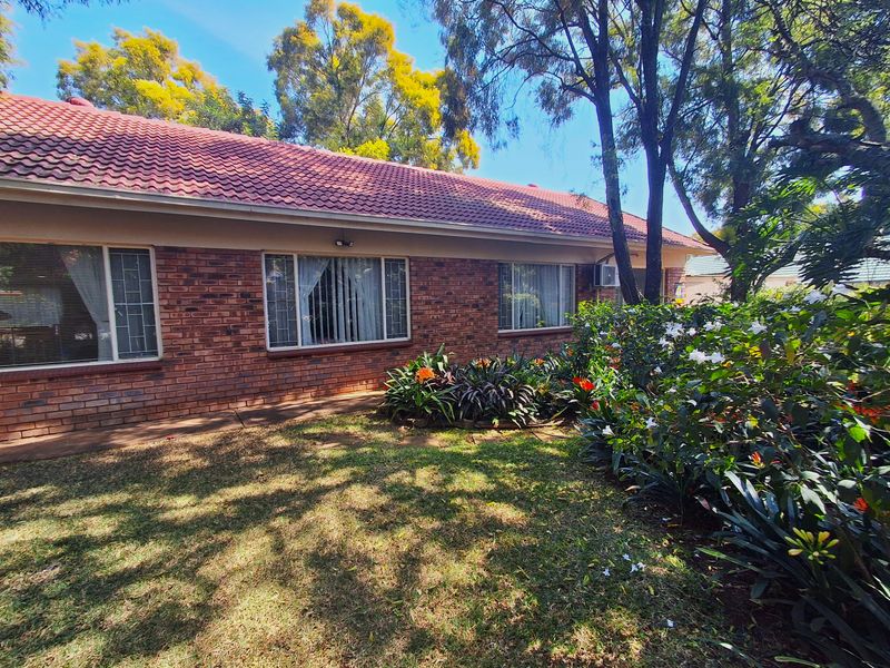 Rear view of a face brick house featuring a tiled roof, established garden, and secure aluminum-framed windows.