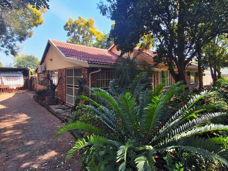 Front view of a brick house featuring a tiled roof, paved driveway, and established garden with a carport.
