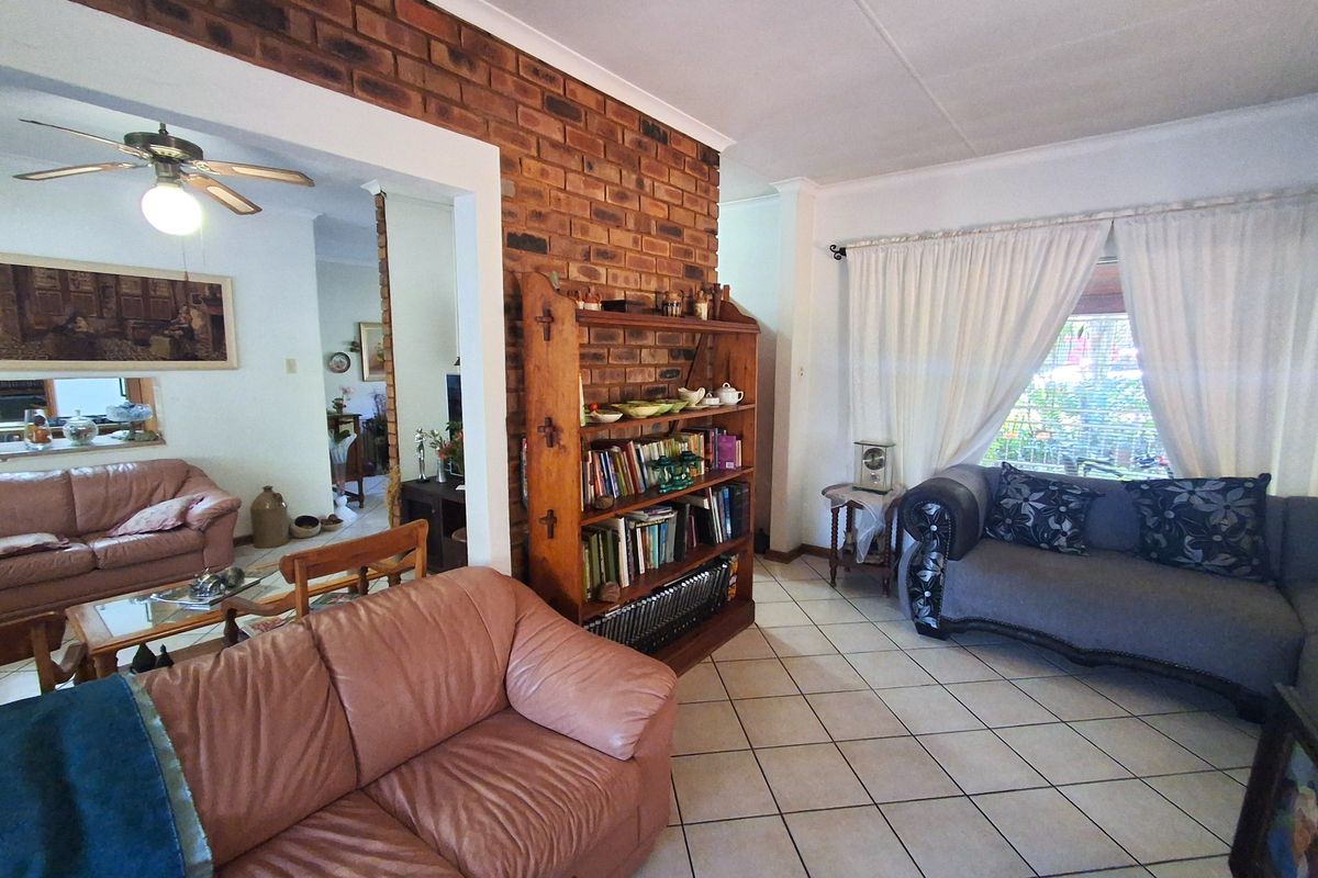 Spacious living area featuring an exposed brick feature wall, tiled flooring, and a ceiling fan, offering a comfortable and traditional layout.