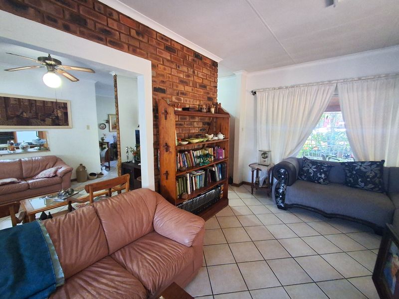Spacious living area featuring an exposed brick feature wall, tiled flooring, and a ceiling fan, offering a comfortable and traditional layout.