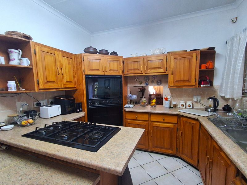 A functional kitchen featuring traditional wooden cabinetry, laminate countertops, a built-in oven, gas hob, and tiled flooring.
