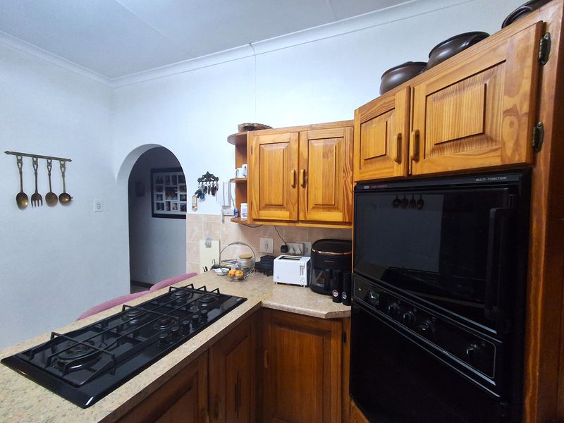 A functional kitchen featuring traditional wooden cabinetry, a built-in gas hob, and an eye-level oven with a tiled backsplash and arched doorway access.