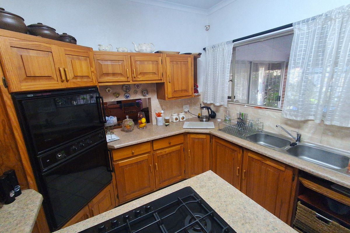 A functional kitchen featuring traditional wooden cabinetry, laminate countertops, a built-in oven, gas cooktop, and a double bowl stainless steel sink.