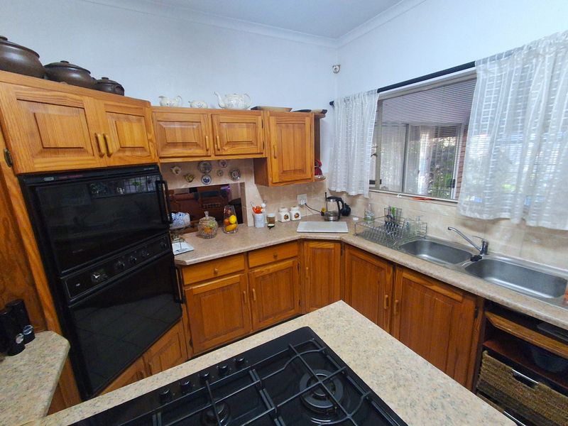 A functional kitchen featuring traditional wooden cabinetry, laminate countertops, a built-in oven, gas cooktop, and a double bowl stainless steel sink.