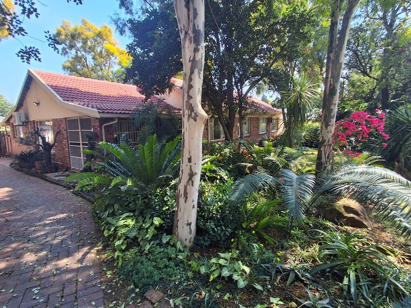 A view of the rear brick facade featuring a tiled roof, paved walkway, and established garden surroundings.