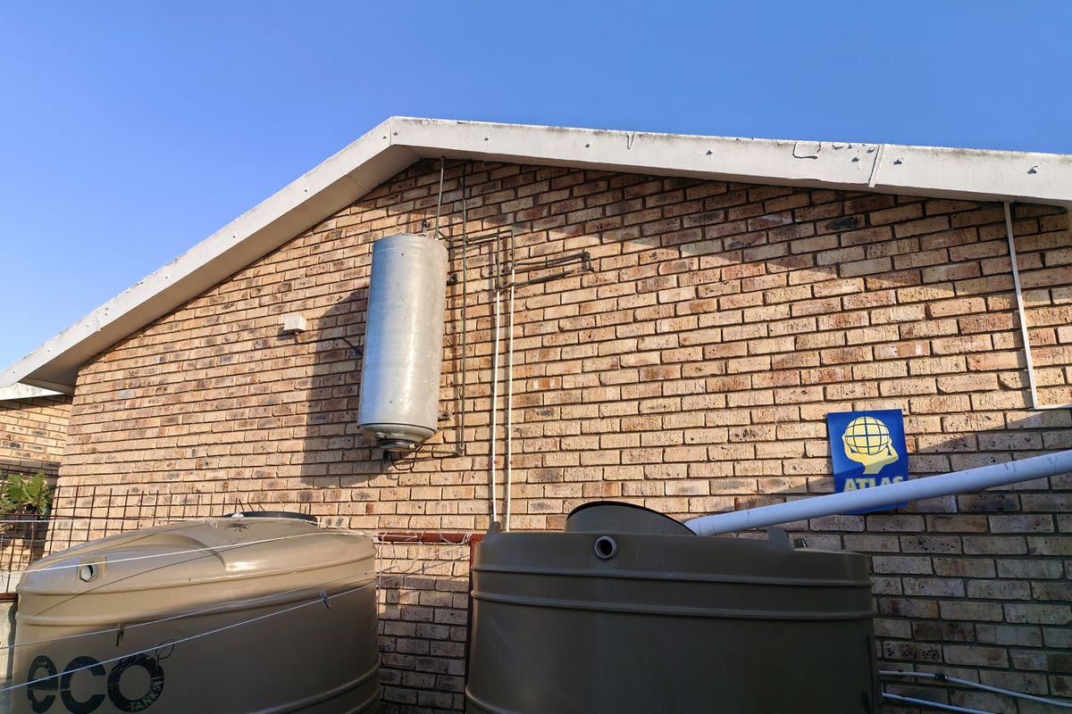 Exterior view of the property featuring brick walling, two large water storage tanks, and an externally mounted electric geyser unit.