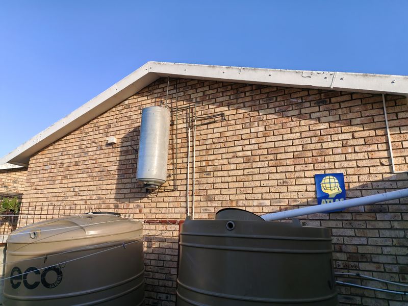 Exterior view of the property featuring brick walling, two large water storage tanks, and an externally mounted electric geyser unit.