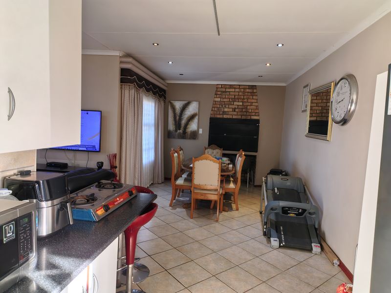 Open-plan living and dining area featuring tiled floors, recessed lighting, and a built-in brick fireplace, seamlessly connected to the kitchen space.
