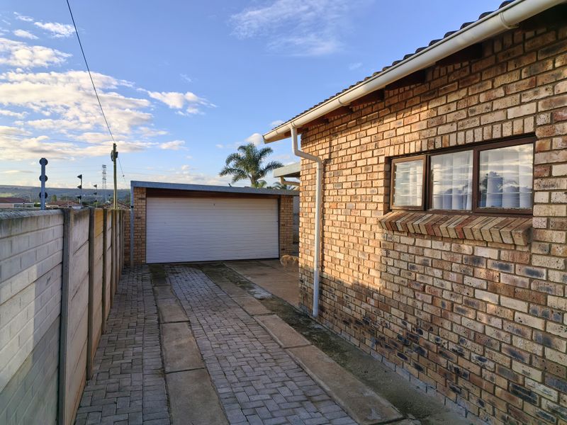 Exterior view of the townhouse featuring a face brick facade, paved driveway, and a secure garage, set against a clear sky.