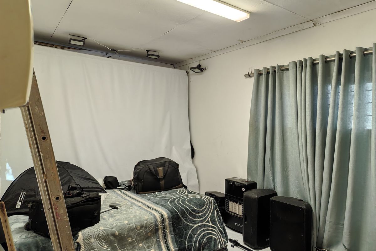A bedroom space featuring a fluorescent ceiling light and curtain rod, currently used as a studio with visible ceiling damage and exposed wiring.