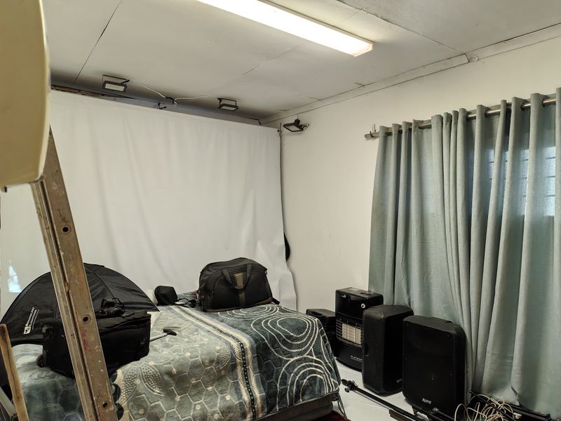 A bedroom space featuring a fluorescent ceiling light and curtain rod, currently used as a studio with visible ceiling damage and exposed wiring.