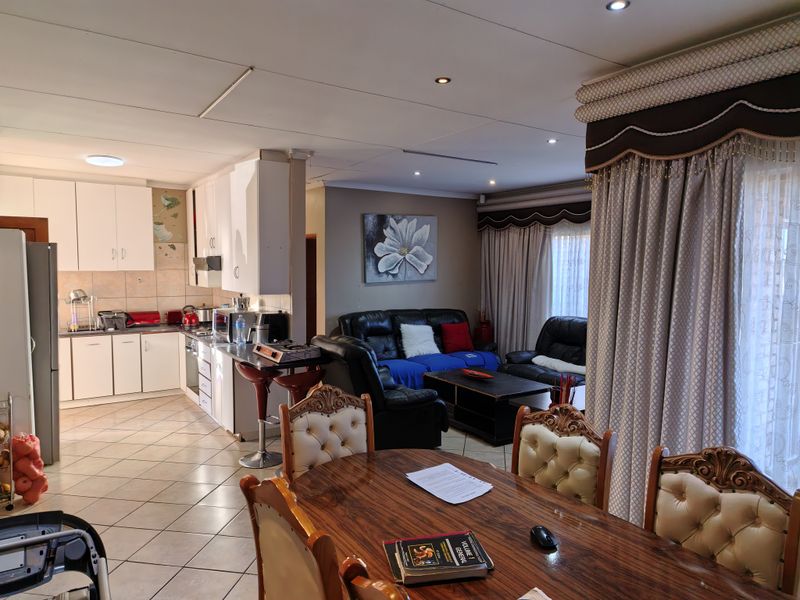 Open-plan living area featuring a functional kitchen with built-in cabinetry, breakfast bar, and tiled flooring, seamlessly flowing into the dining and lounge space.