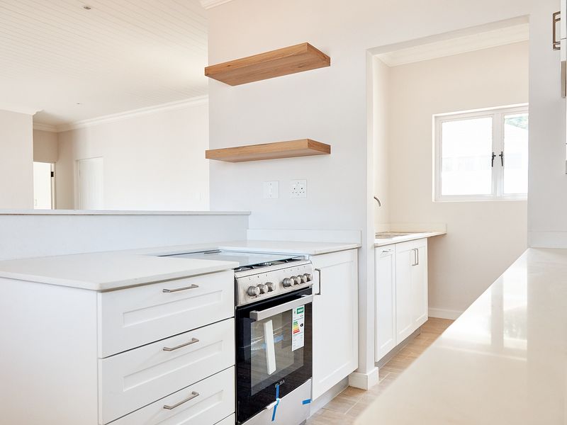 Modern kitchen featuring white cabinetry, stone countertops, a freestanding oven, and floating timber shelves, with an adjacent scullery area.