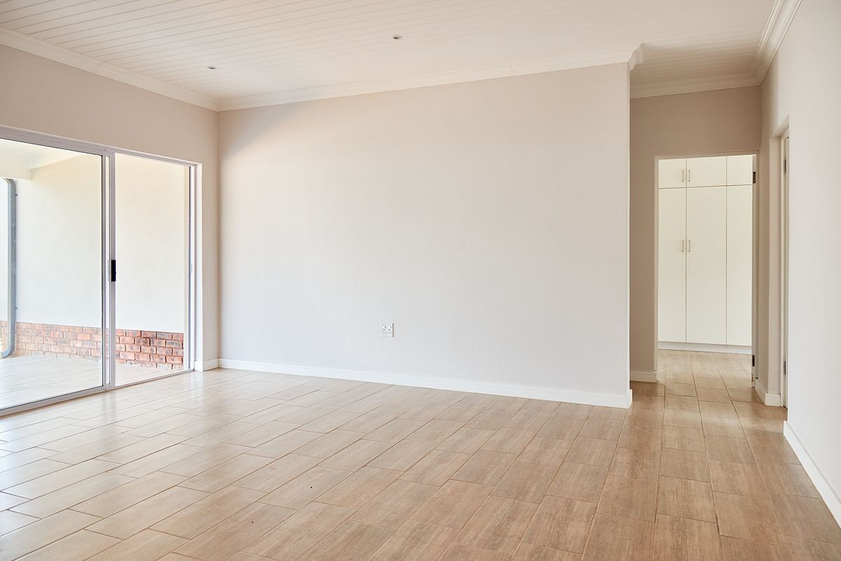 A bright, empty living area featuring modern wood-look tiled flooring, recessed ceiling lights, and a sliding door leading to an outdoor patio space.