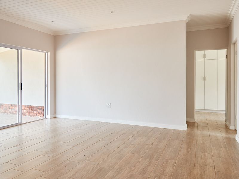 A bright, empty living area featuring modern wood-look tiled flooring, recessed ceiling lights, and a sliding door leading to an outdoor patio space.