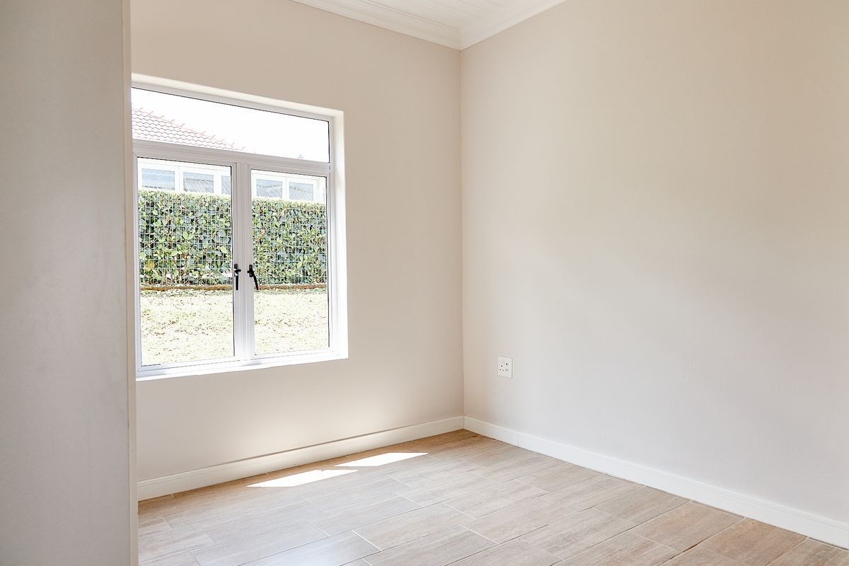 A bright, empty bedroom featuring neutral walls, tiled flooring, and a large window overlooking the garden area.
