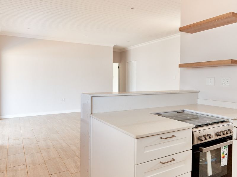 Bright open-plan living area featuring a modern kitchen with stone countertops, gas hob, built-in oven, and seamless access to the outdoors via sliding doors.