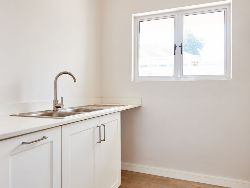 A clean and modern scullery area featuring white cabinetry, a stainless steel double sink with a gooseneck faucet, and a bright window.
