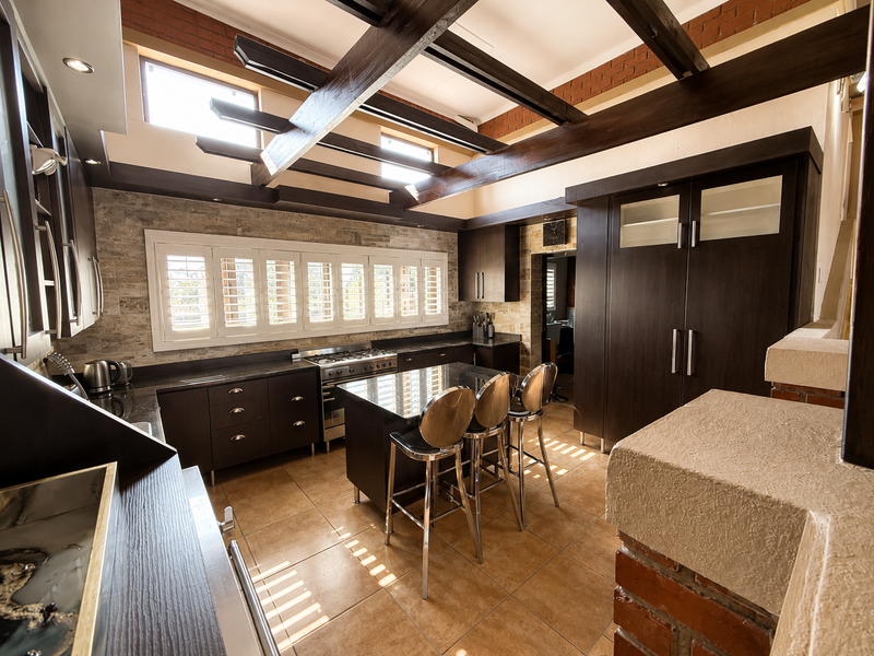 Modern kitchen featuring dark cabinetry, a central island, exposed timber beams, and stone tile accents, creating a warm and functional culinary space.