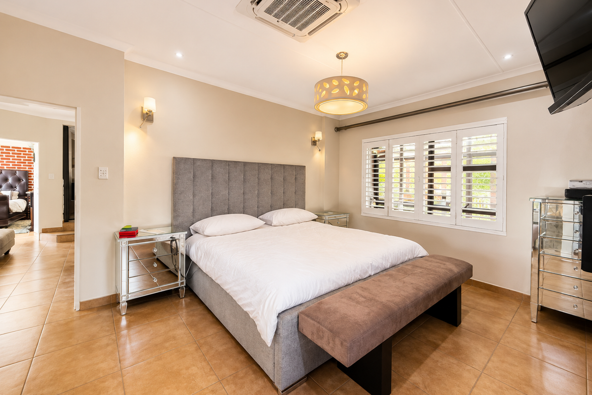 Spacious bedroom featuring tiled flooring, plantation shutters, and a ceiling-mounted air conditioning unit, providing a comfortable and well-maintained living space.