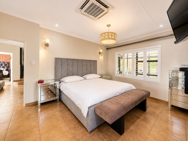 Spacious bedroom featuring tiled flooring, plantation shutters, and a ceiling-mounted air conditioning unit, providing a comfortable and well-maintained living space.