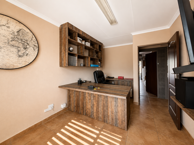 A functional home office featuring built-in wood-look cabinetry, a matching desk, and durable ceramic floor tiles.