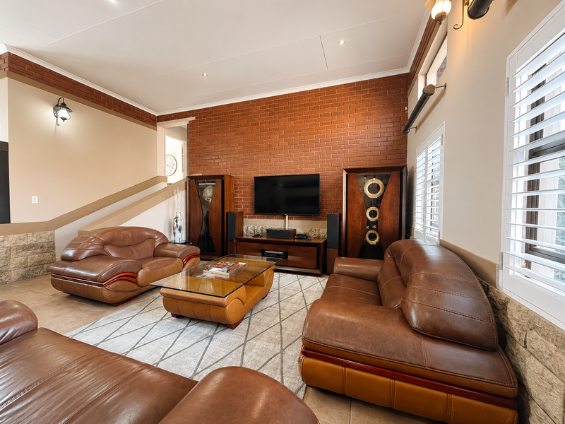 Spacious living room featuring an exposed brick feature wall, tiled flooring, and plantation shutters, creating a warm and inviting atmosphere.