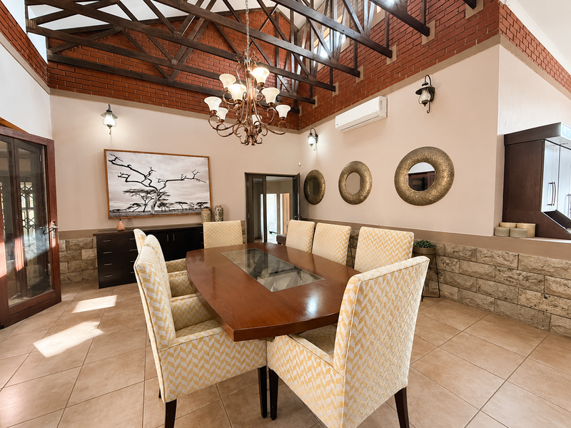 Spacious dining room featuring high vaulted ceilings with exposed timber trusses, exposed brick accents, stone wall cladding, and tiled flooring.