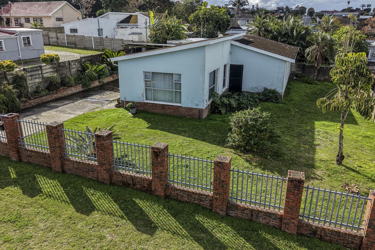 Aerial view of a residential property featuring a brick perimeter wall, metal fencing, concrete driveway, and a single-story house with a tiled roof.