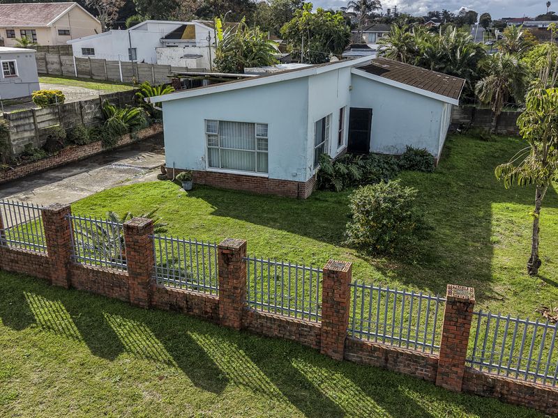 Aerial view of a residential property featuring a brick perimeter wall, metal fencing, concrete driveway, and a single-story house with a tiled roof.