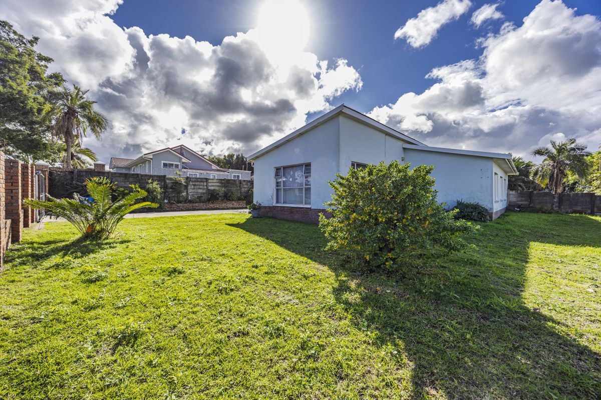 Rear view of the property featuring a spacious lawn, brick boundary walls, and the rear facade of the house.
