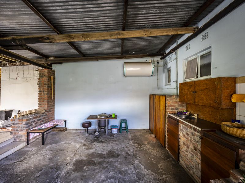 A rustic covered patio area featuring exposed brickwork, timber beams, a corrugated roof, and basic built-in cabinetry with a sink.