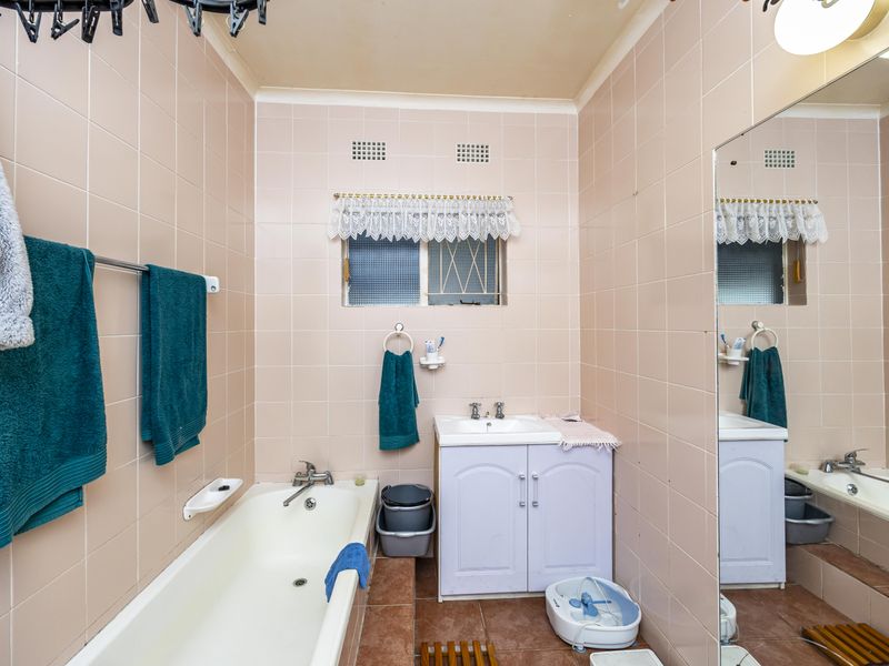 A dated bathroom featuring pink wall tiles, a built-in vanity, and a standard bathtub with a large wall mirror.