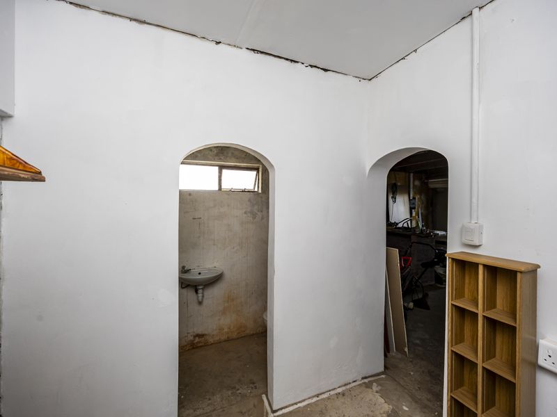 A utility area featuring arched doorways, a wall-mounted basin, and exposed infrastructure, requiring cosmetic updates and finishing to improve functionality and aesthetic appeal.