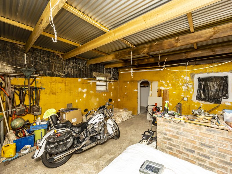 A rustic garage space featuring exposed timber rafters, a corrugated metal roof, and unfinished brick and masonry walls with visible electrical wiring.