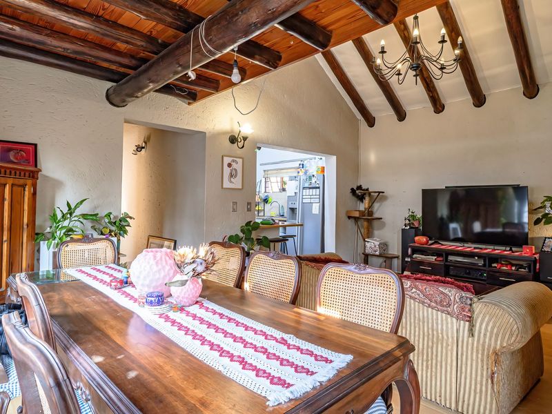Open plan living and dining area featuring vaulted ceilings with exposed timber beams, warm timber flooring, and a classic chandelier.