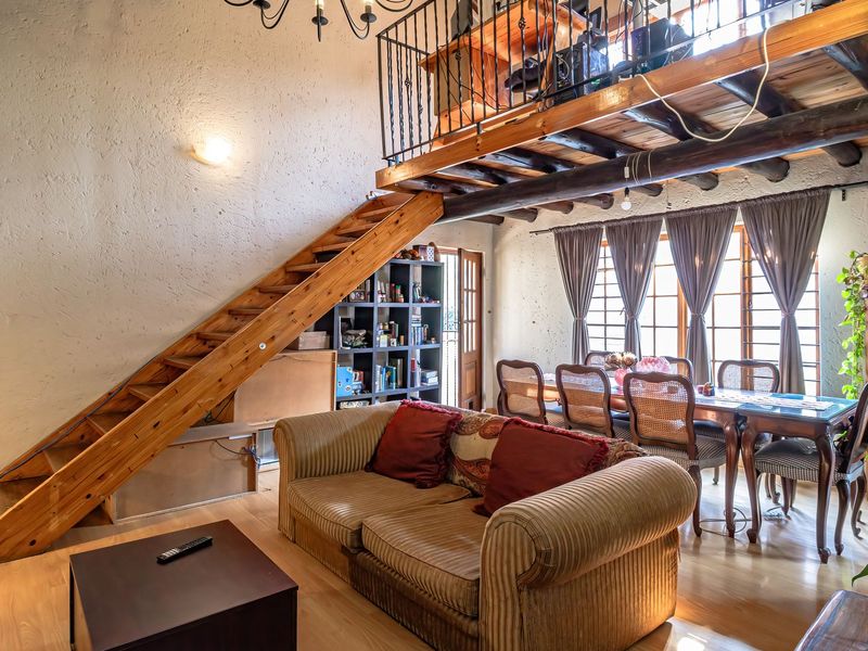 Open-plan living and dining area featuring a mezzanine level, exposed timber beams, wooden staircase, and large windows providing natural light.