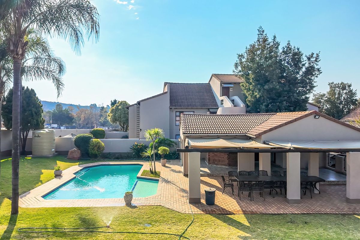 Spacious rear exterior featuring a swimming pool, paved patio area with overhead cover, and well-maintained garden space within a secure complex.