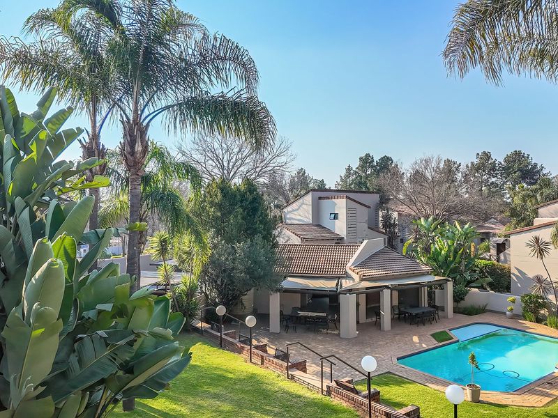 Rear view of the property featuring a swimming pool, covered patio area, and well-maintained garden with mature palm trees.