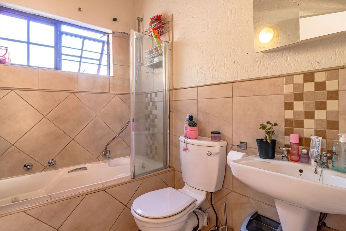 A functional bathroom featuring a bathtub with a glass shower screen, a pedestal basin, and a toilet, finished with neutral wall and floor tiling.