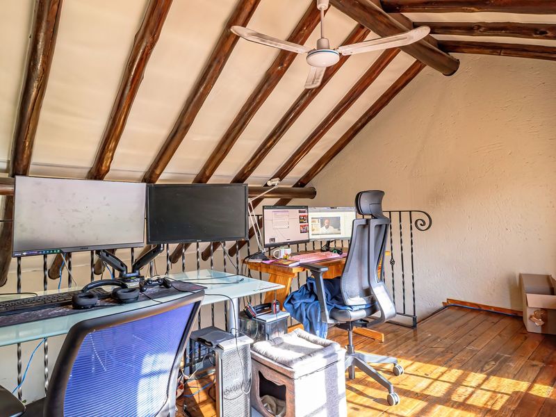 A loft-style office space featuring exposed timber rafters, wooden flooring, and a decorative wrought iron balustrade overlooking the lower level.