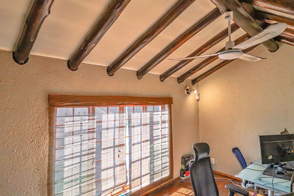 A bedroom featuring a vaulted ceiling with exposed timber beams, a ceiling fan, and a large window with textured wall finishes.