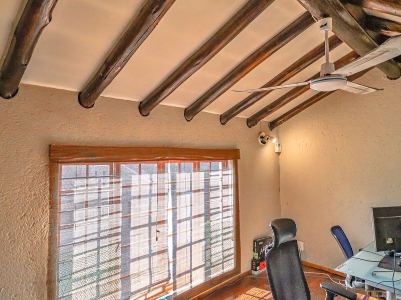 A bedroom featuring a vaulted ceiling with exposed timber beams, a ceiling fan, and a large window with textured wall finishes.