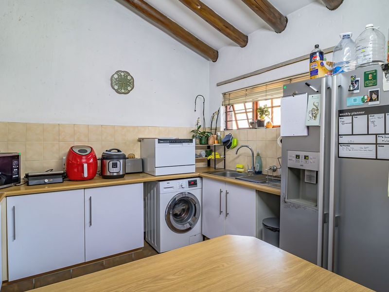 A functional kitchen featuring exposed timber ceiling beams, tiled backsplash, laminate countertops, and integrated laundry plumbing.