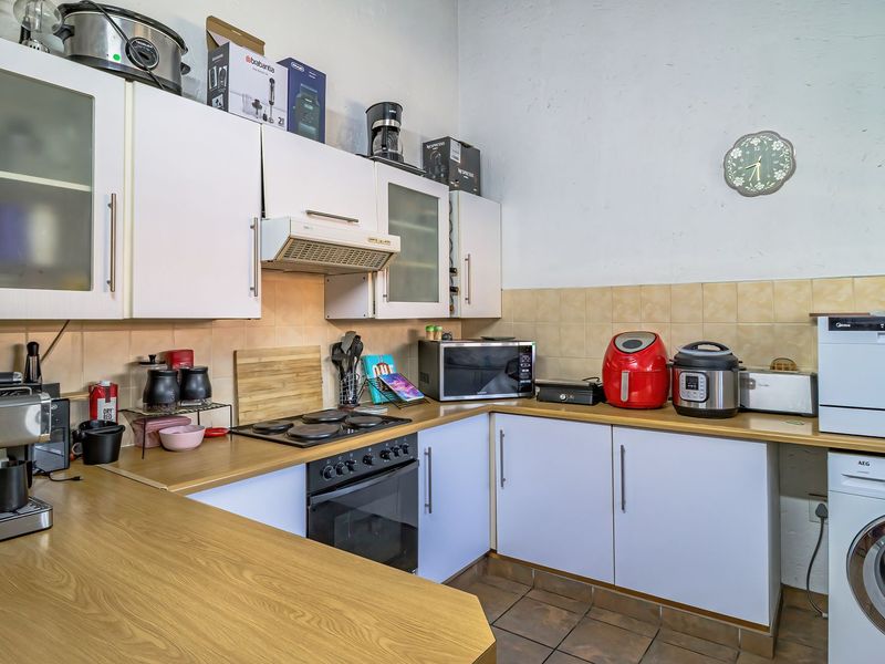 A functional kitchen featuring white cabinetry, wood-look laminate countertops, tiled backsplash, and integrated appliances including an oven, hob, and washing machine.