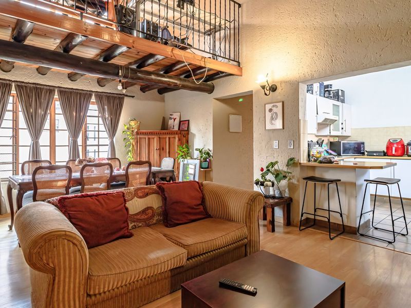 Open-plan living and dining area featuring a mezzanine level with timber beams, integrated kitchen with breakfast bar, and laminate flooring throughout.