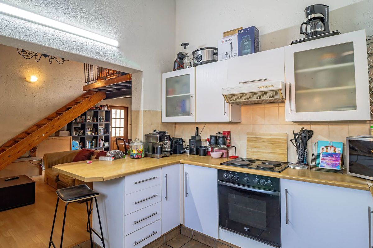 A functional kitchen featuring white cabinetry, laminate countertops, and built-in appliances, with an open-plan layout leading to a staircase area.