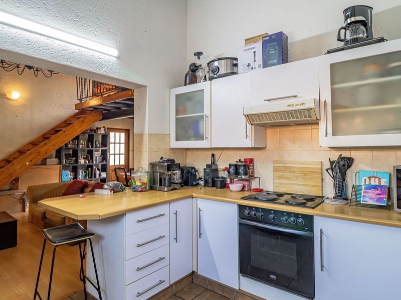 A functional kitchen featuring white cabinetry, laminate countertops, and built-in appliances, with an open-plan layout leading to a staircase area.