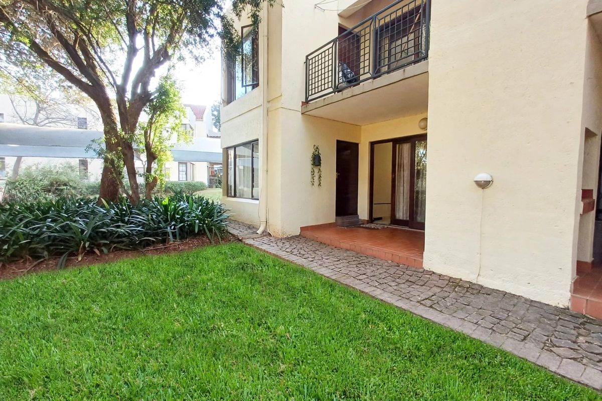 Rear view of the townhouse featuring a private garden, paved walkway, and an upper-level balcony with metal railings.
